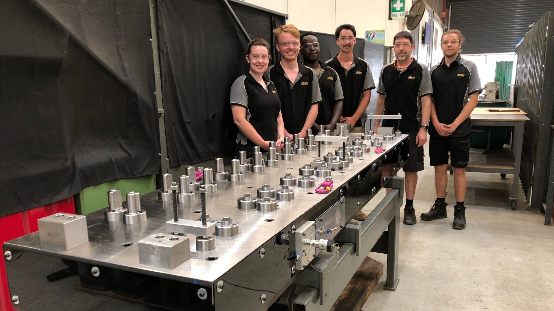 Five people from Axiom standing around a long table with space parts